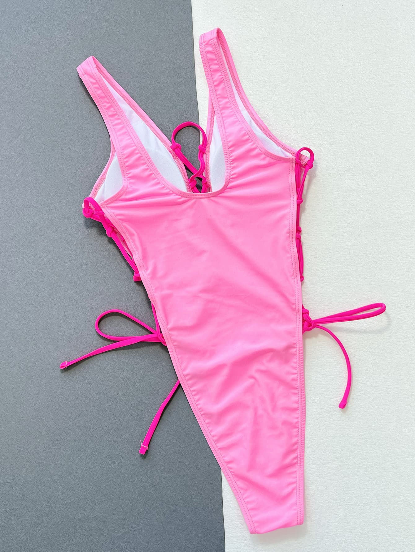 Pink Deep V Lace up one piece swimsuit on flat white/gray surface back view