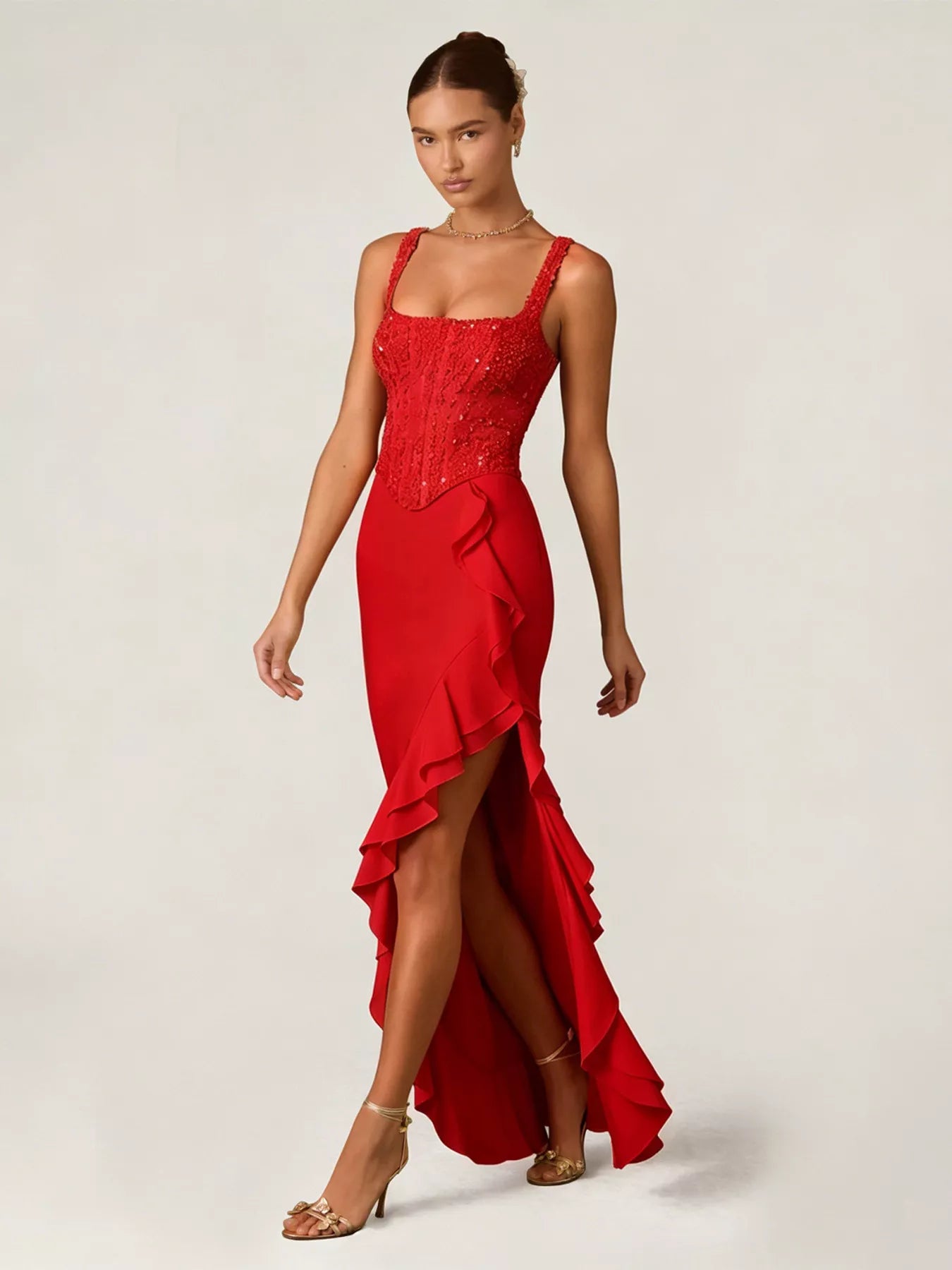 Woman wearing a red gown with sequin detailing top and ruffled skirt on a white background front view