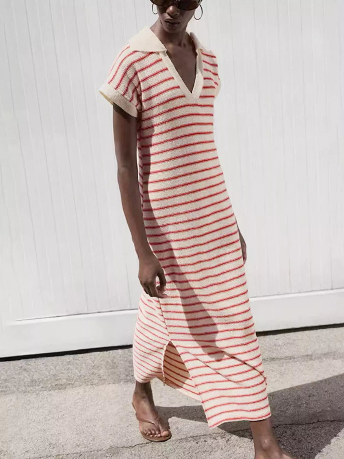 Woman wearing a red and white striped dress against a white wall.