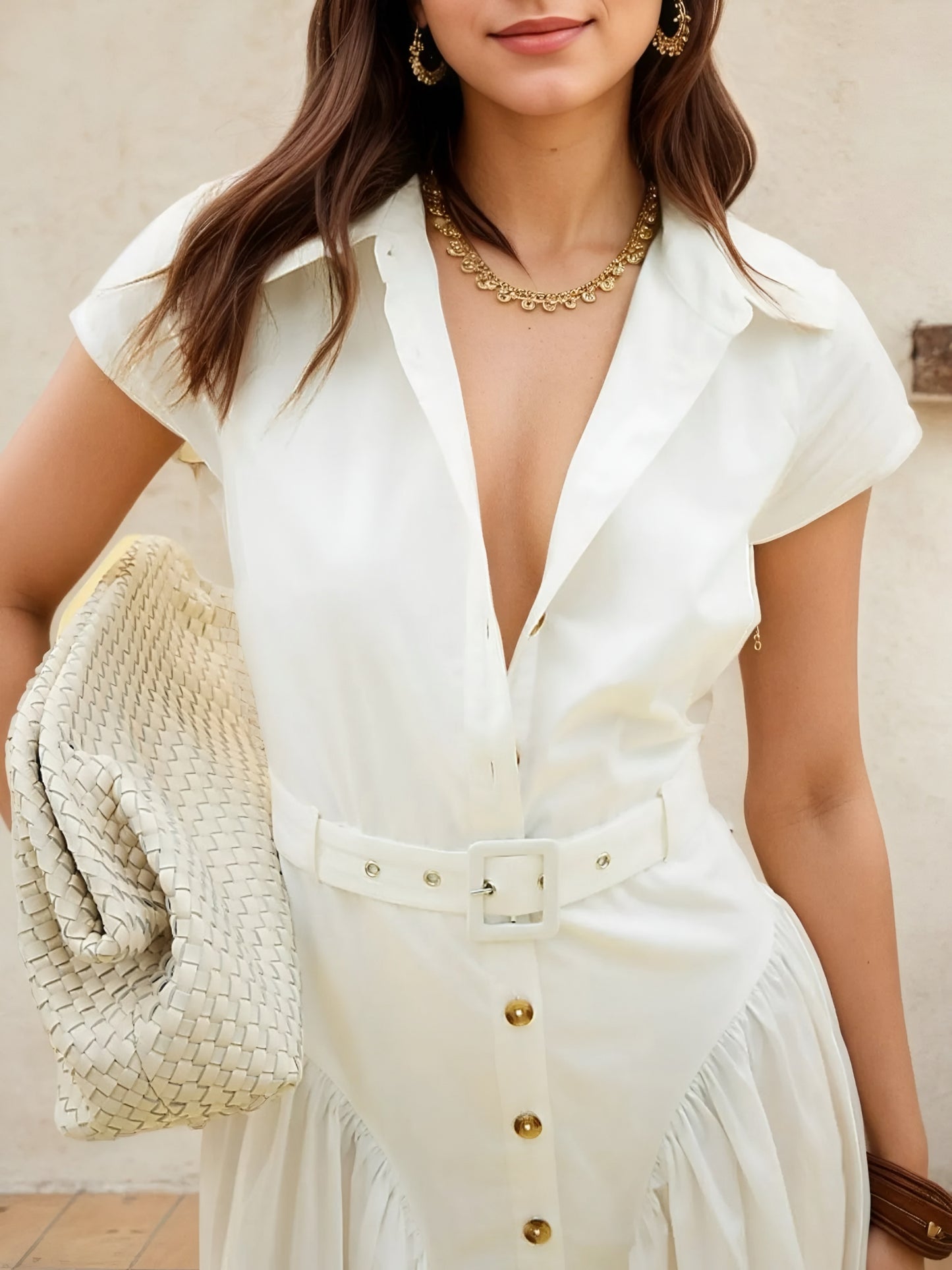 Woman wearing a white belted button front cap sleeve midi casual shirt dress with a deep neckline, holding a beige woven bag.