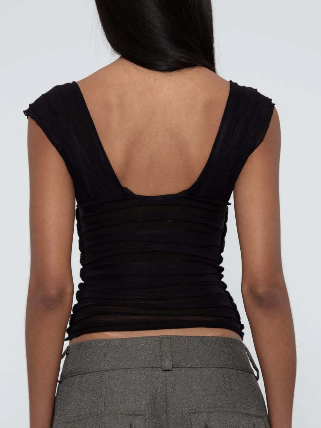 woman wearing a black sleeveless ruched top back view and gray pants on a white background