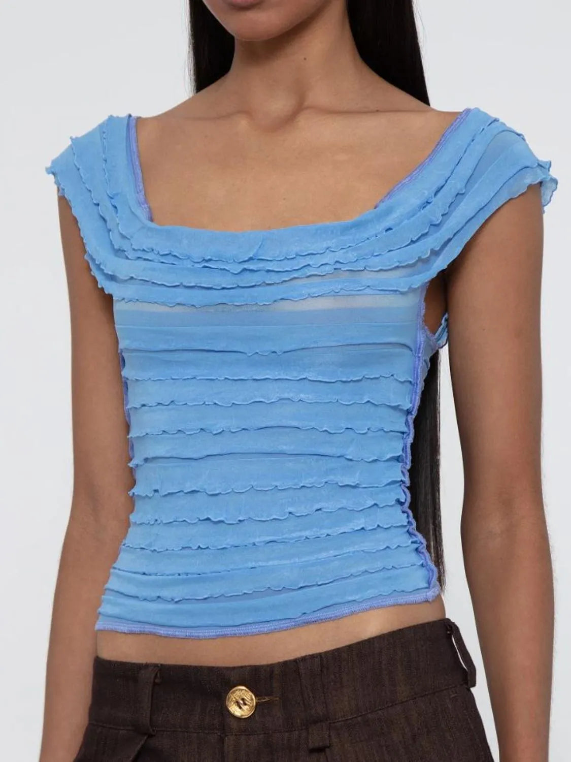 Blue ruffled ruched sleeveless top worn by a woman on a white background