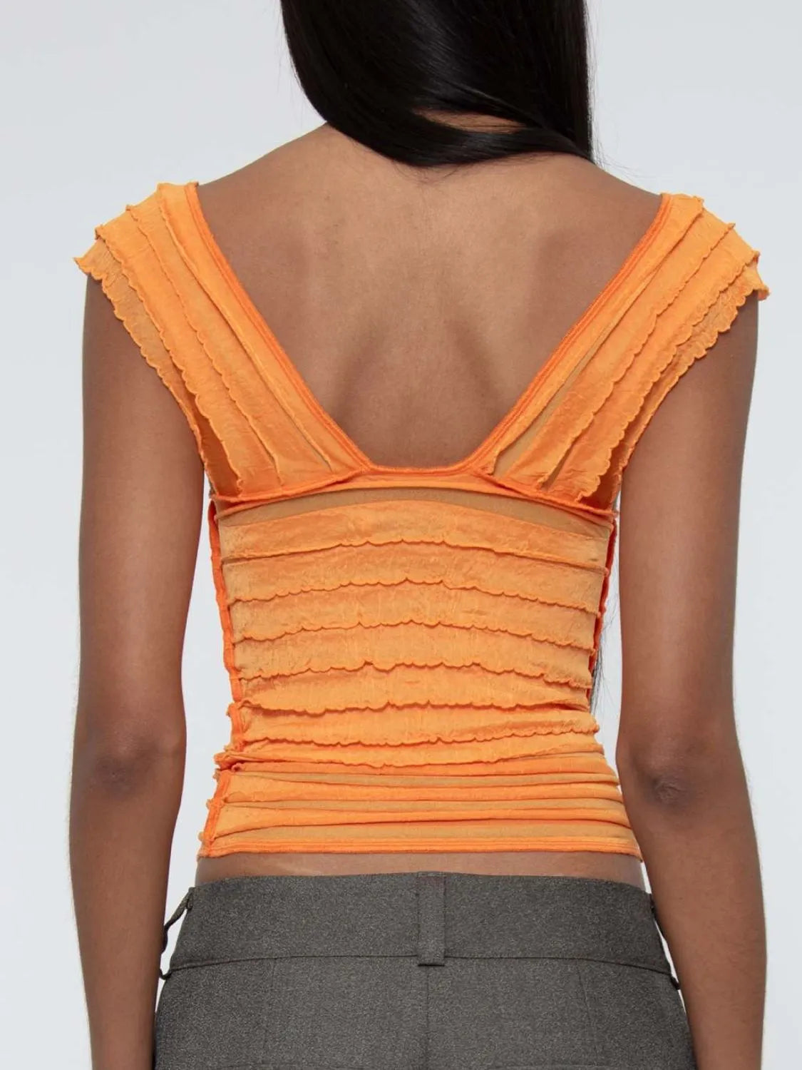 Orange ruffled ruched sleeveless top worn by a woman back view on a plain background