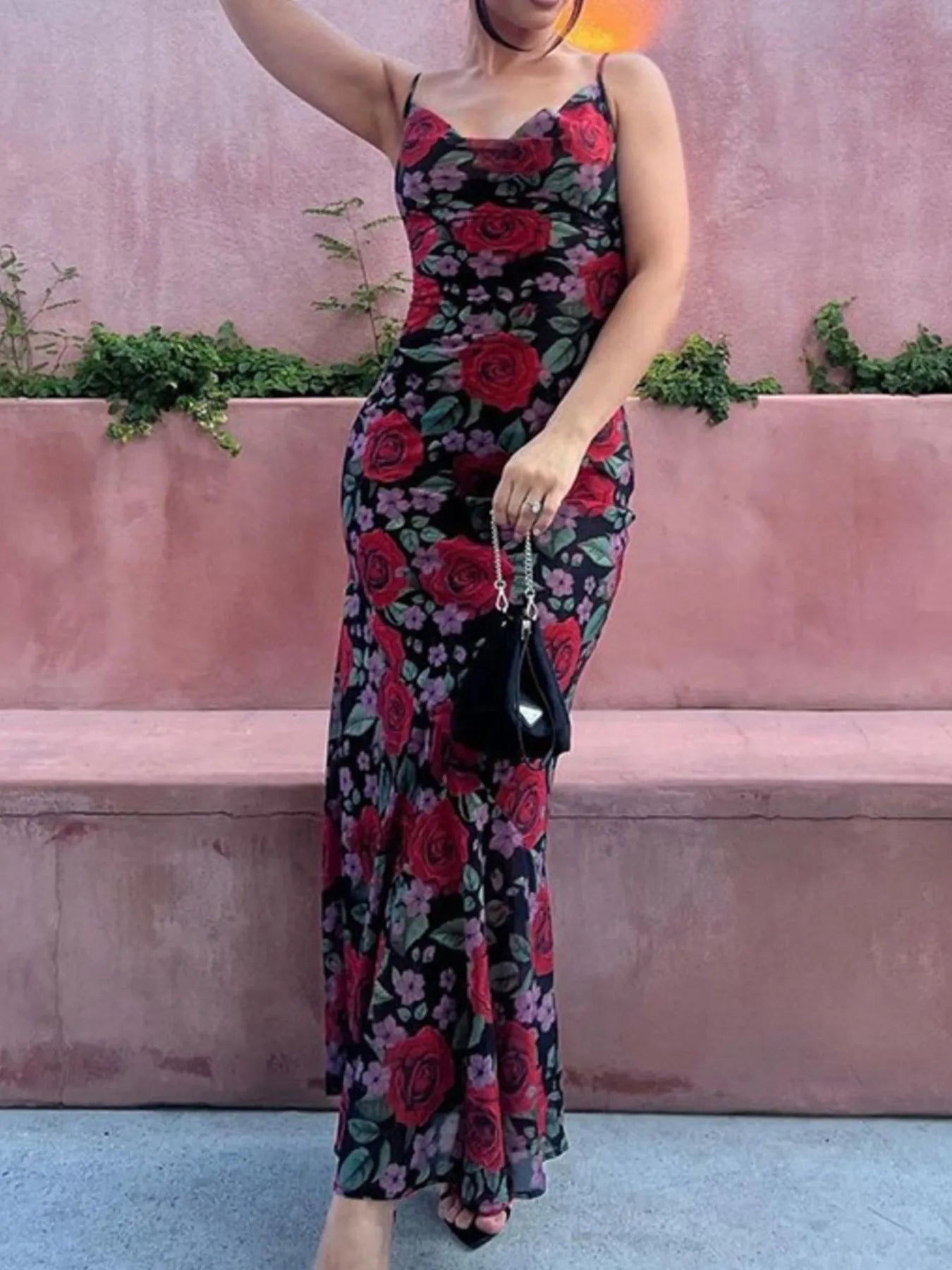 woman wearing a floral maxi dress against a pink wall with green plants.