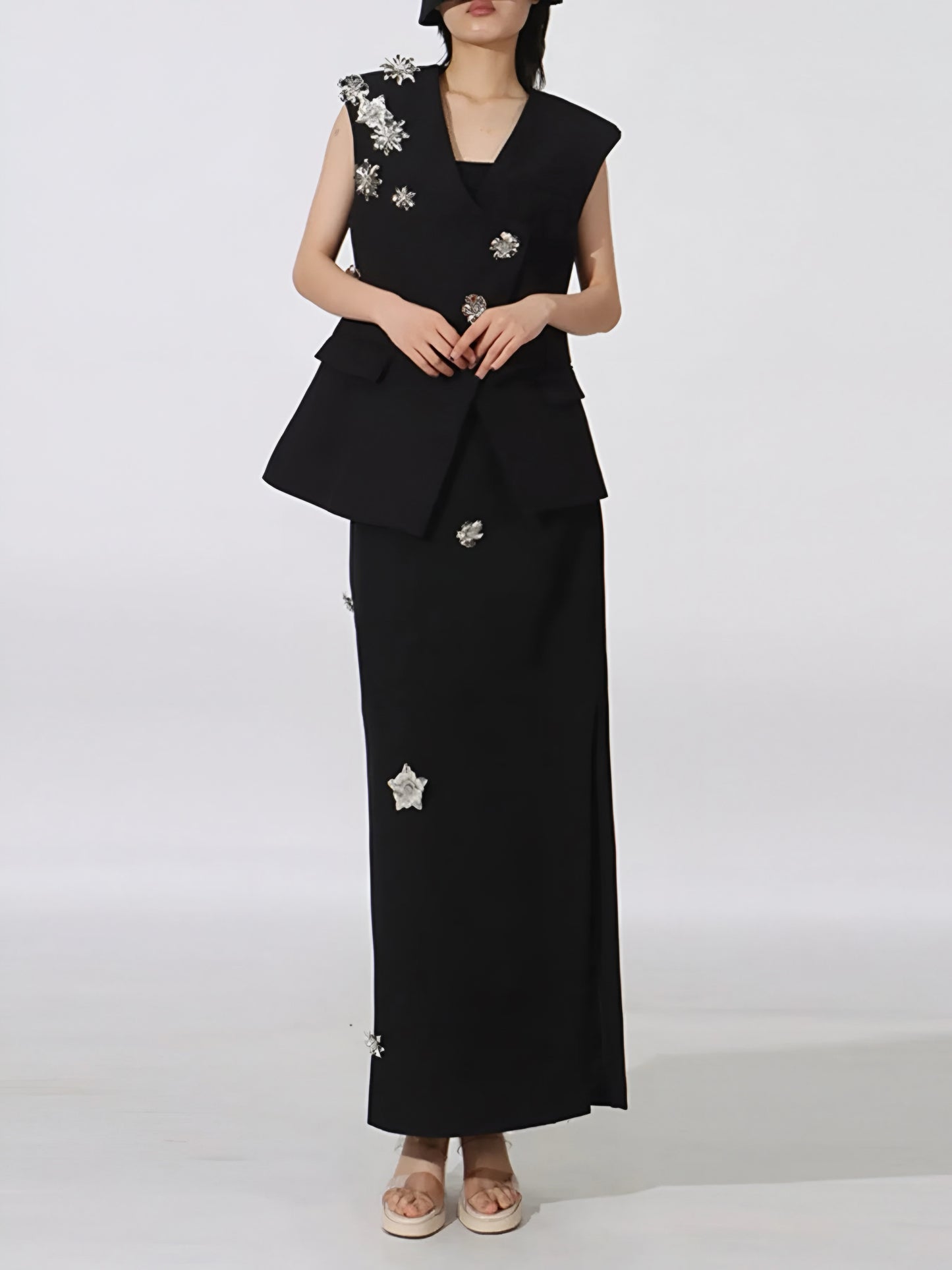 Woman wearing a black Designer-inspired two-piece co-ord with tailored vest and maxi skirt with floral embellishments on a white background