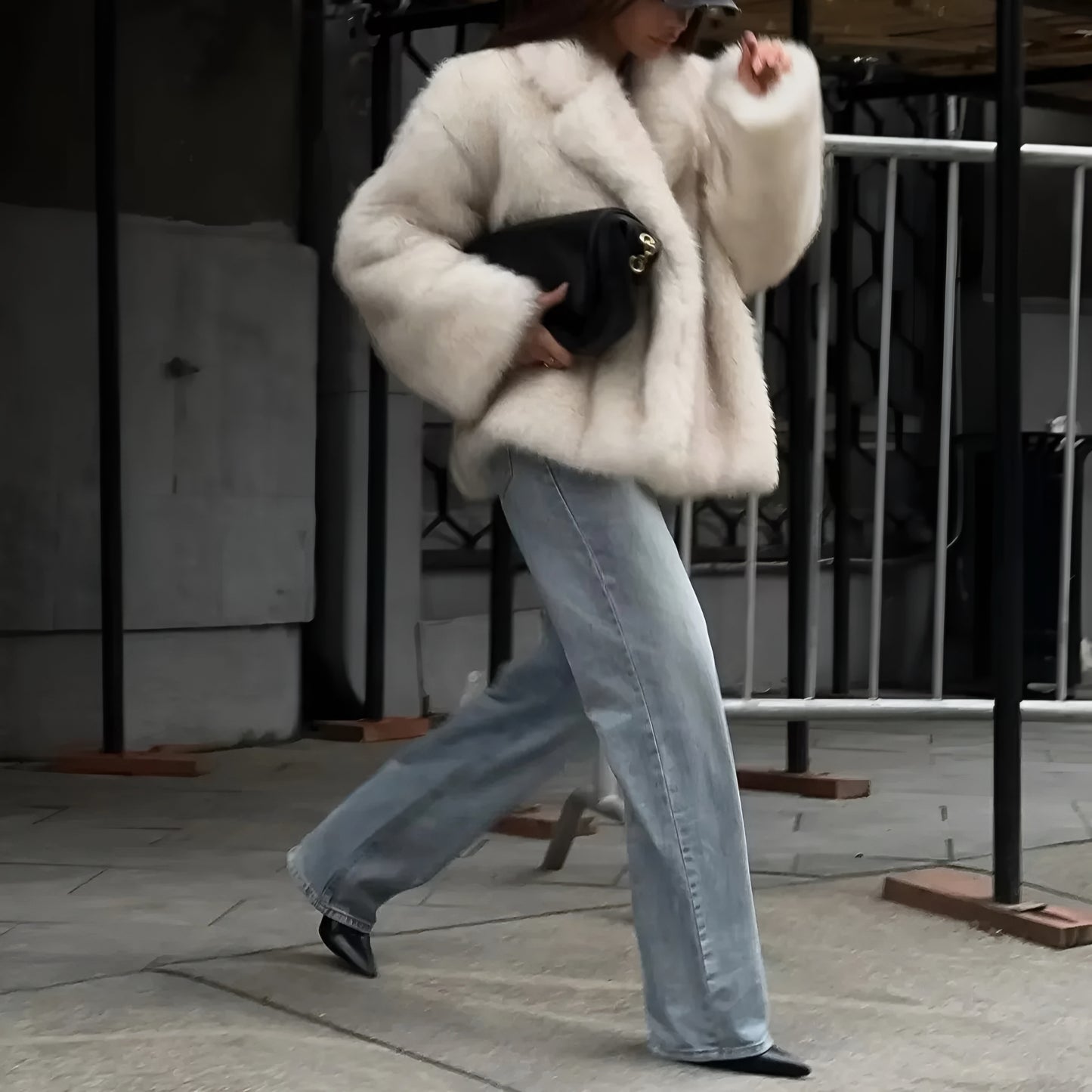 Woman wearing a white high-end women’s fashion plush fur coat with tailored silhouette with light blue jeans walking outdoors.