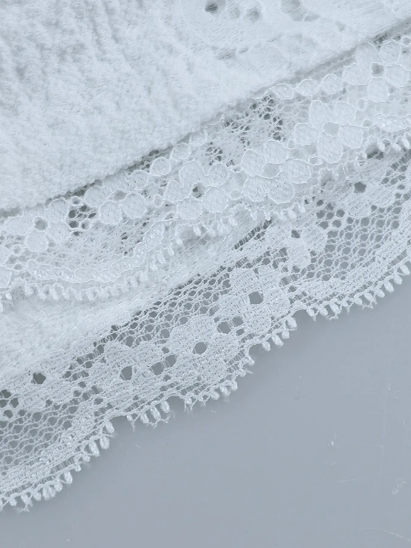 Close-up of white lace fabric hem of Lace Off-Shoulder Maxi Dress with Flounce Sleeves on a light gray background