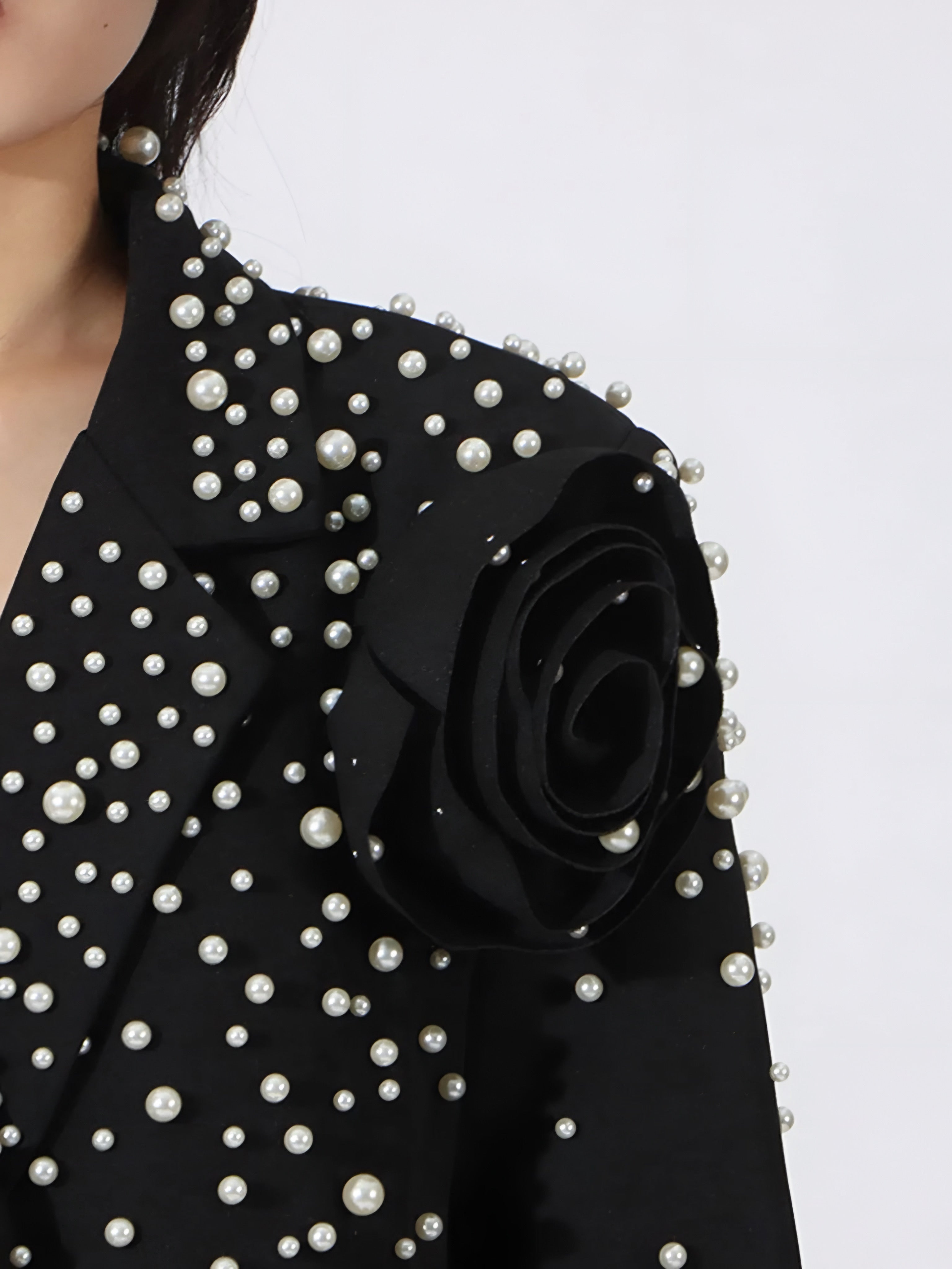 Close up of shoulder of black couture-inspired pearl blazer on a white background