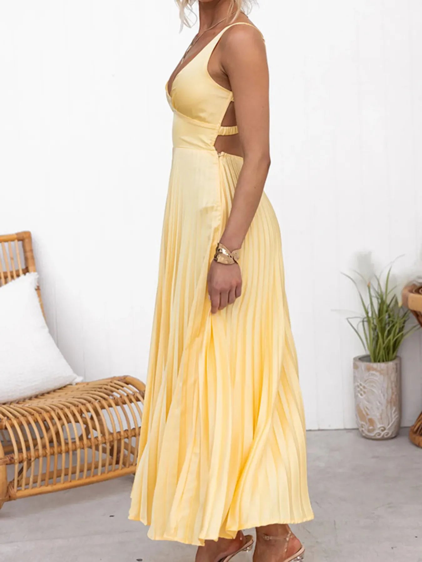 Side view of woman wearing a yellow backless flowy maxi formal dress in a minimal indoor setting.