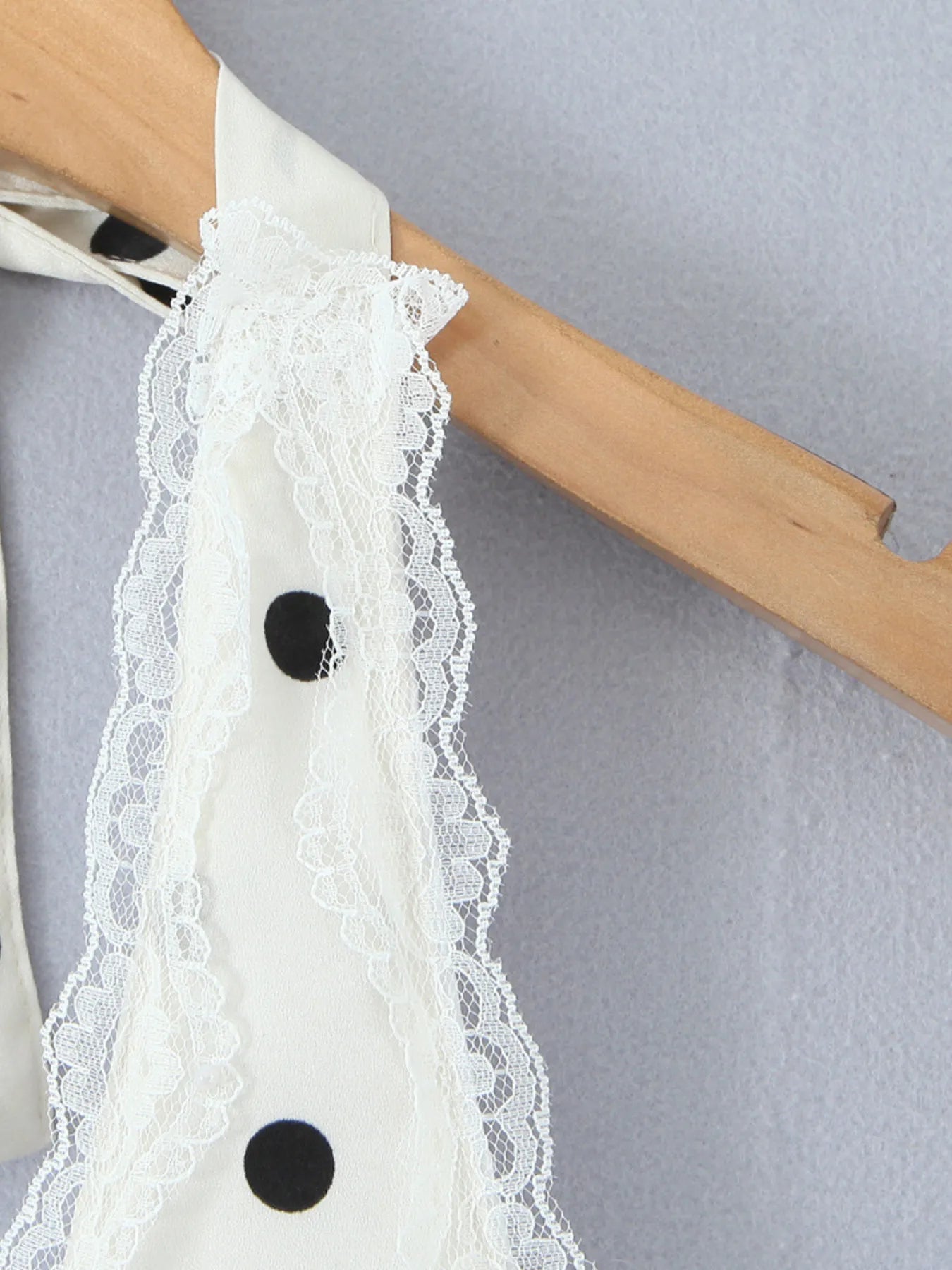 Close-up of lace trim at neckline of polka dot halter mini dress hanging on wooden hanger