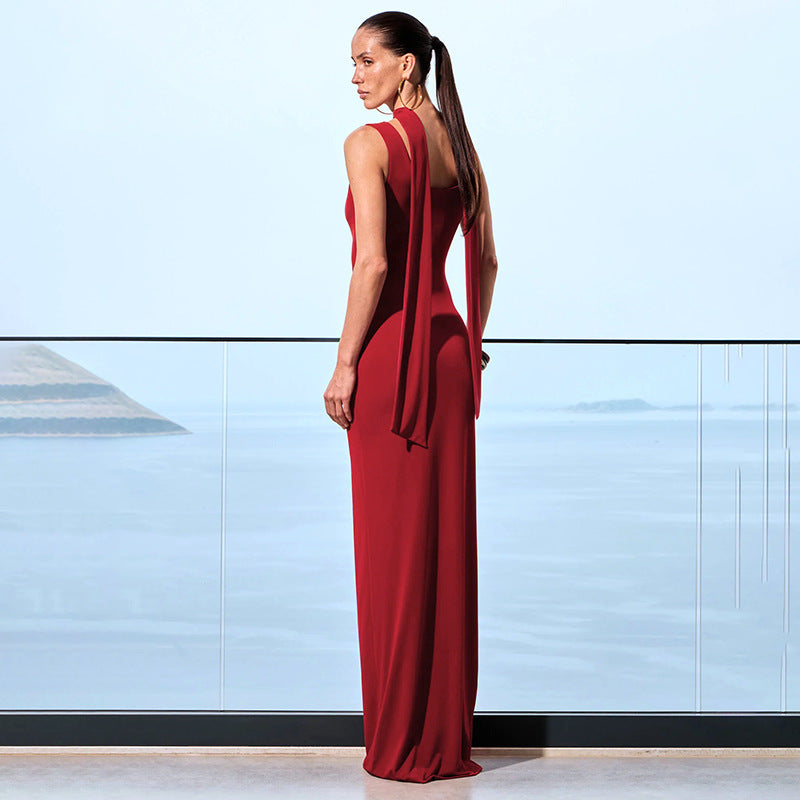 Back view of woman wearing a red cutout detail evening gown standing against a light blue wall.