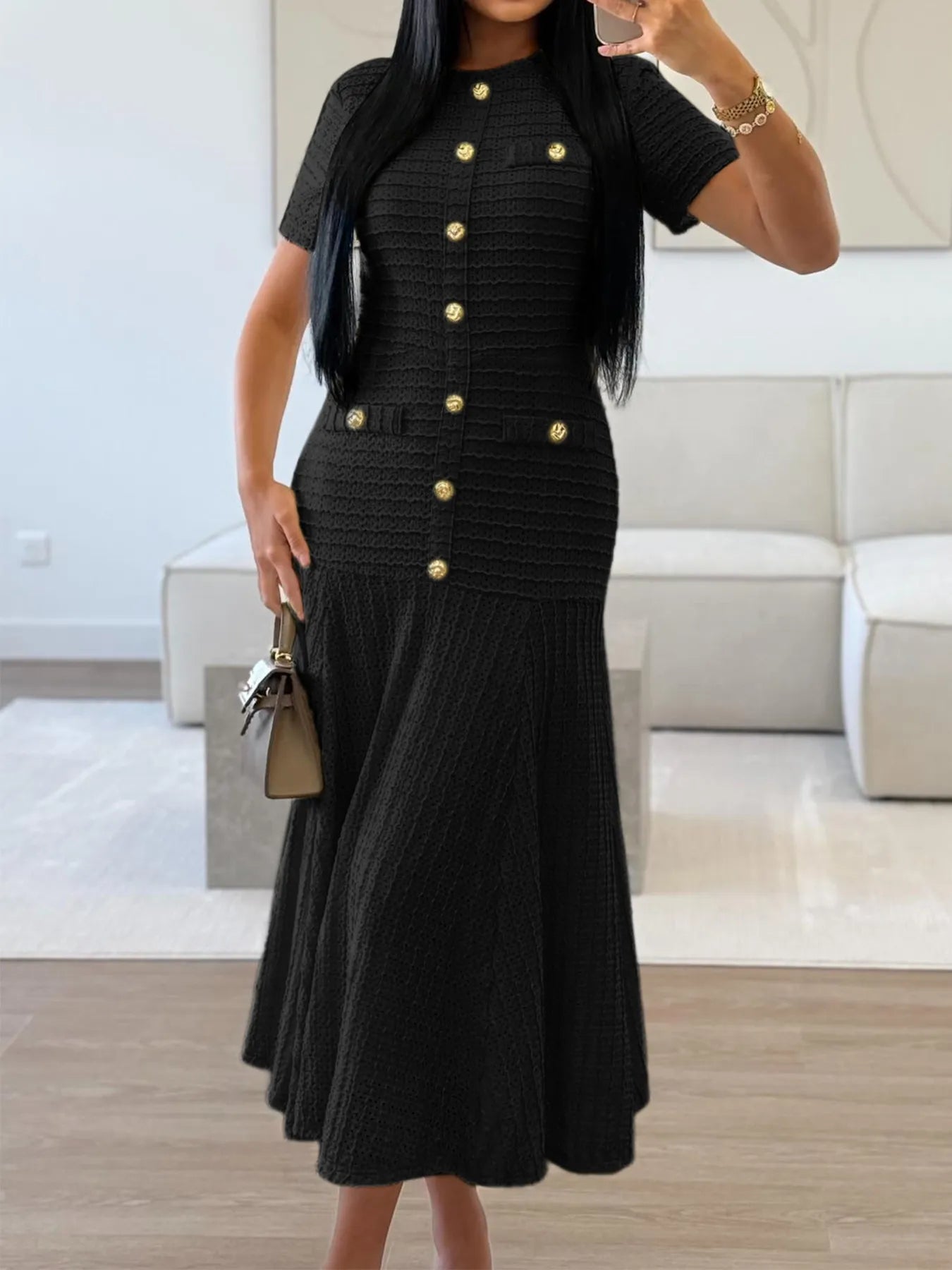 Woman wearing a black Textured Knit Short Sleeve Midi Dress with gold buttons in an indoor setting