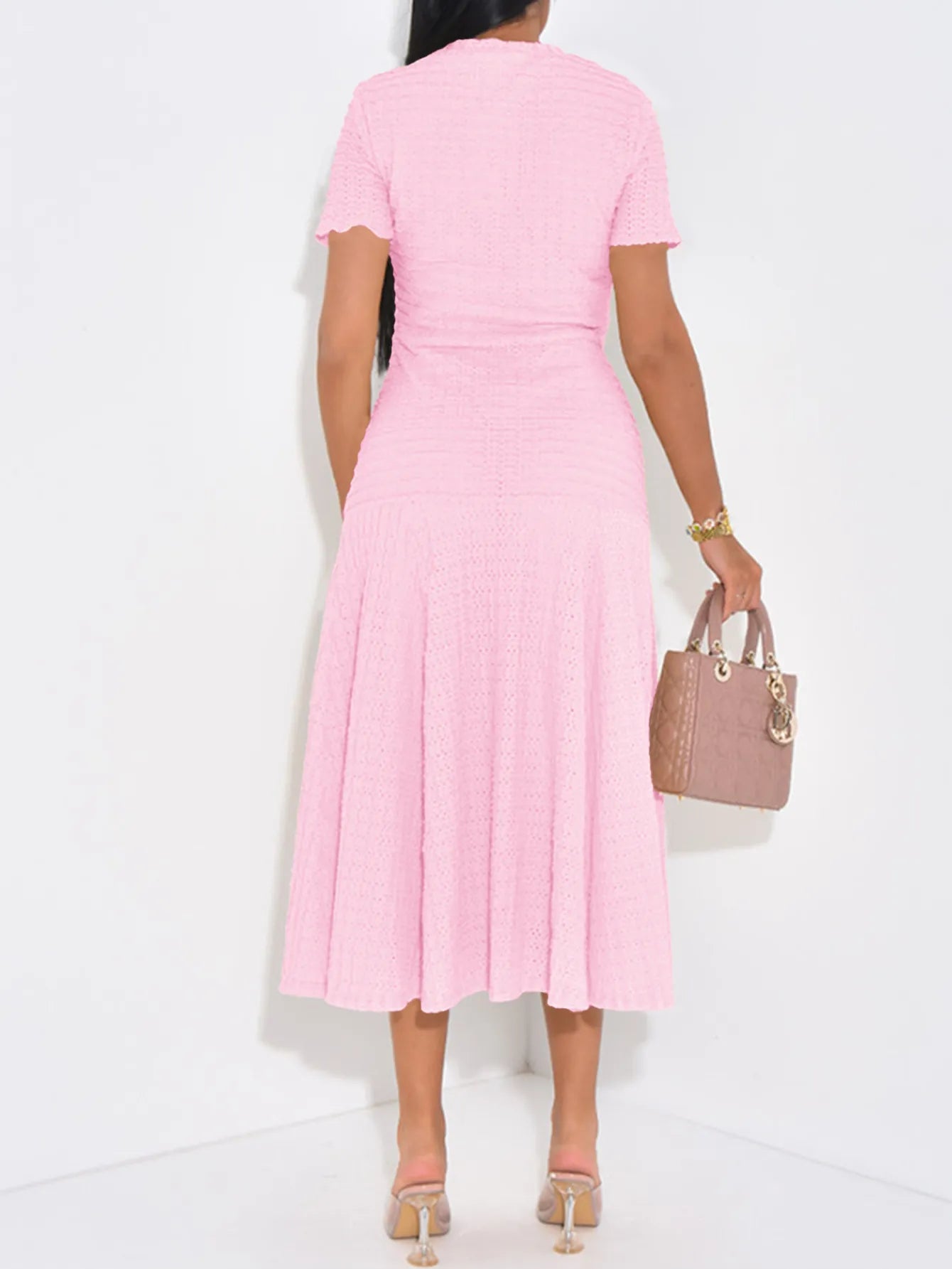 Back view of woman wearing a pink Textured Knit Short Sleeve Midi Dress holding a matching handbag against a white background