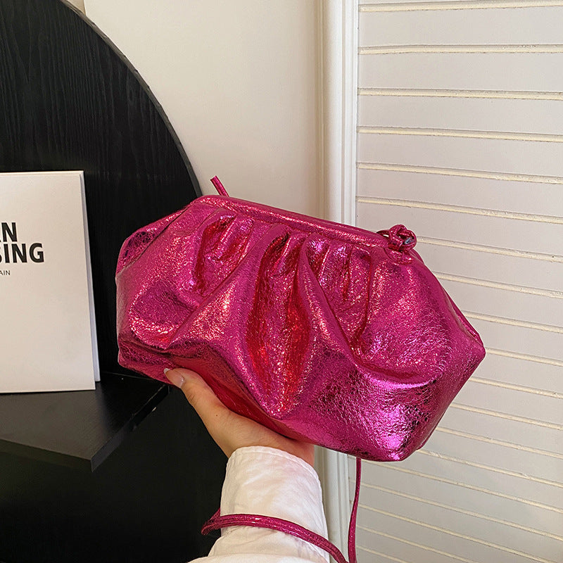 Woman holding a metallic hot pink colored PU leather clip shell bag with detachable strap.