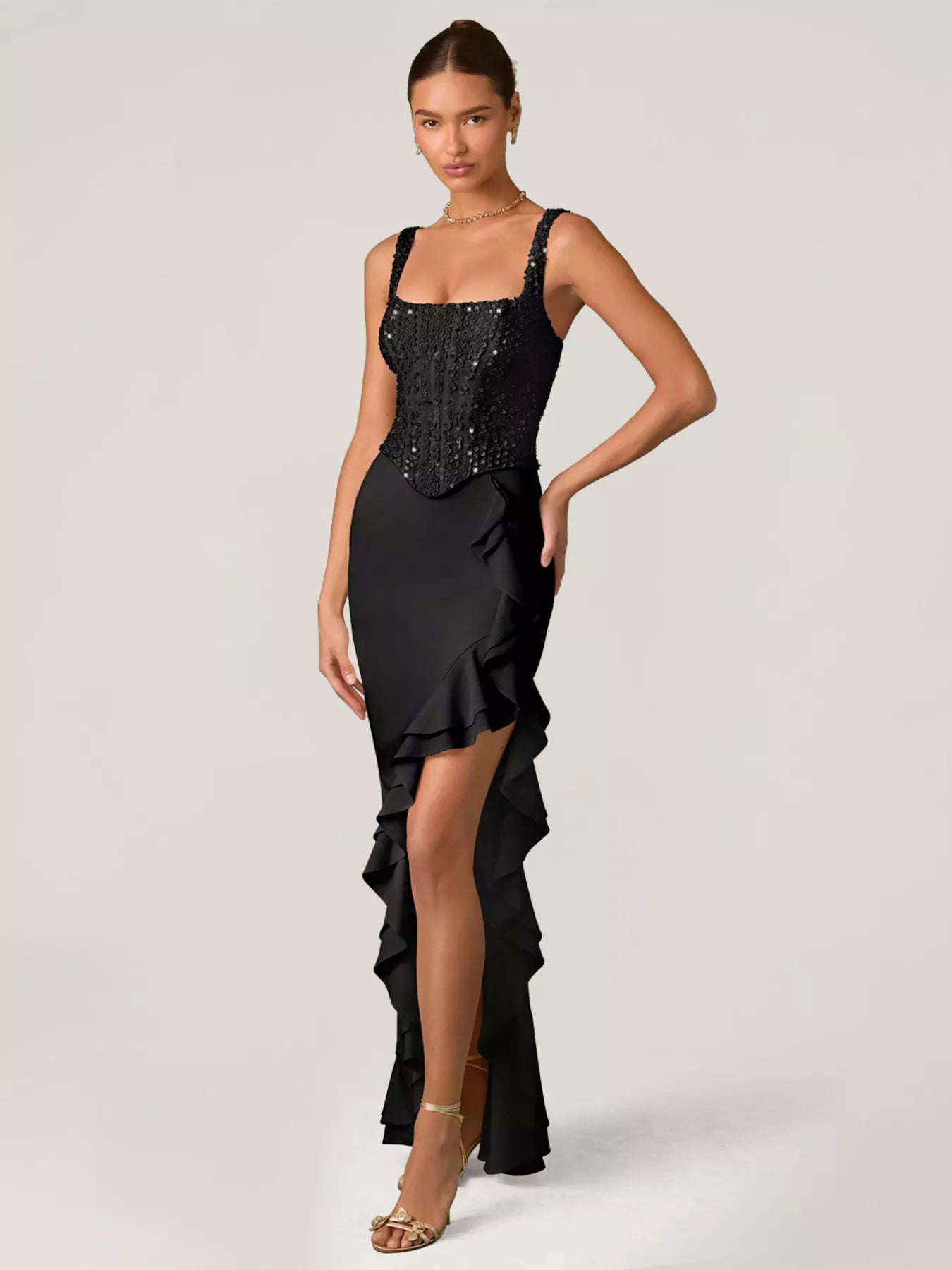 Woman wearing a black evening gown with sequin detailing top and ruffled skirt on a white background front view