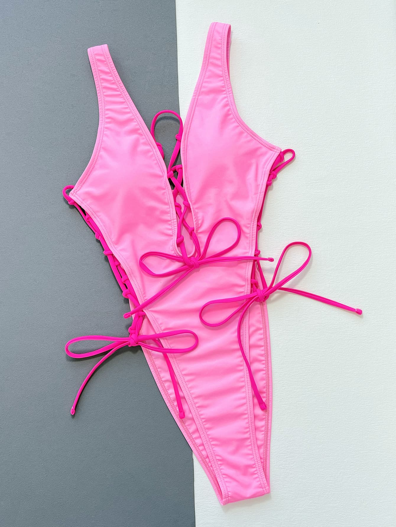 Pink Deep V Lace up one piece swimsuit on flat white/gray surface front view