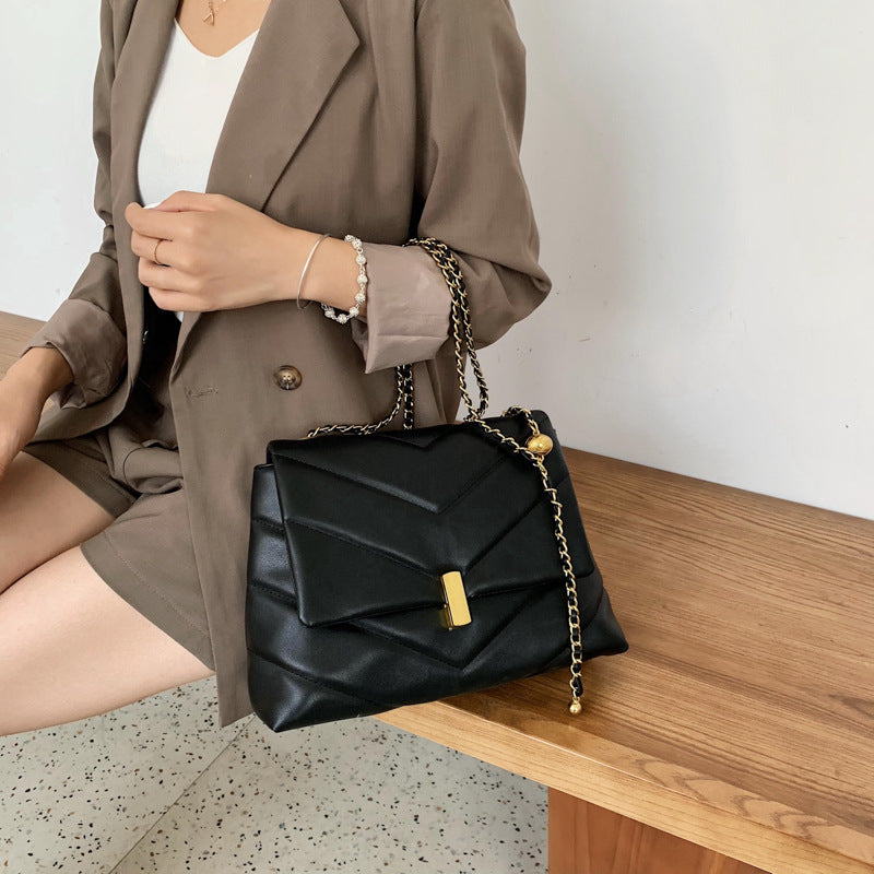 Woman holding black quilted chain chevron shoulder bag with gold clasp sitting on a bench