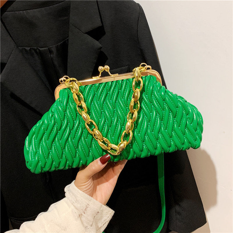 Green textured leather clutch handbag with gold chain handle held by a woman wearing a black coat.