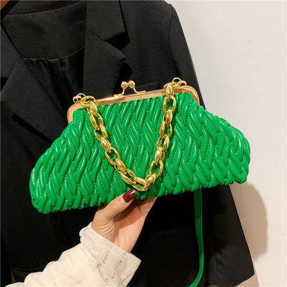 Green textured leather clutch handbag with gold chain handle held by a woman wearing a black coat.