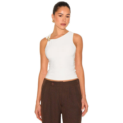Woman wearing a white sleeveless top with gold clasp and brown pants on a white background