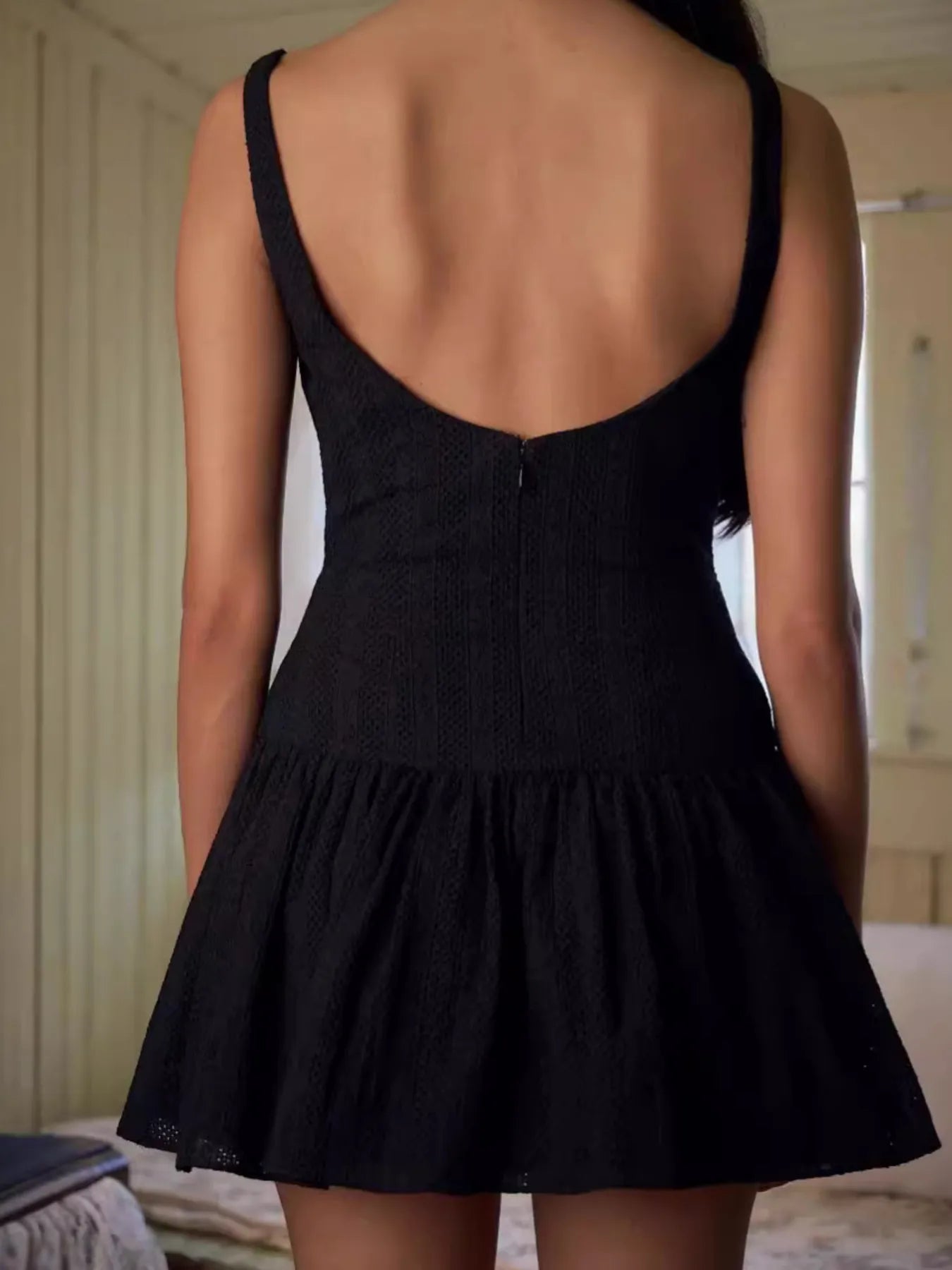 Model wearing black sleeveless lace bodycon mini dress in white back view with zipper
