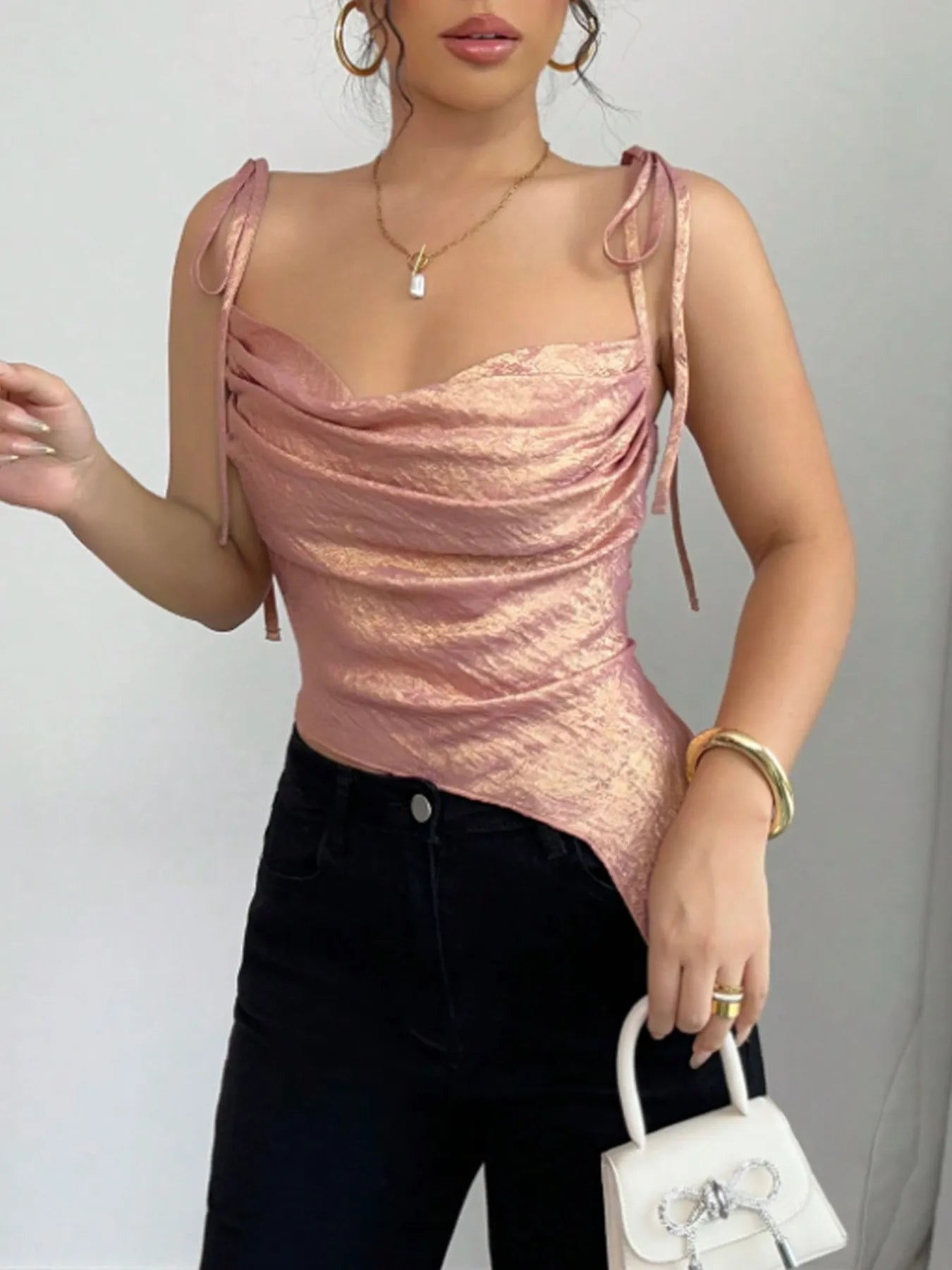 Woman wearing a pink summer cami top and black pants, holding a white handbag against a gray background