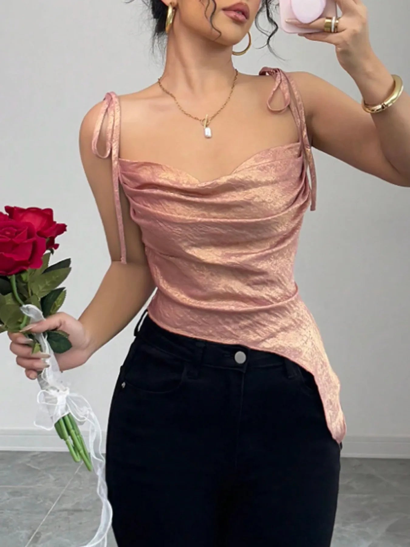 Woman wearing a pink cami summer trendy top and black pants, holding a red rose.