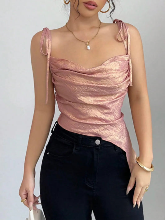 Woman wearing a pink tie shoulder summer cami top and black pants against a gray background