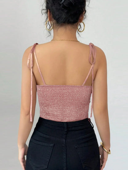 woman wearing a pink cami top with thin tie up adjustable straps on a plain background