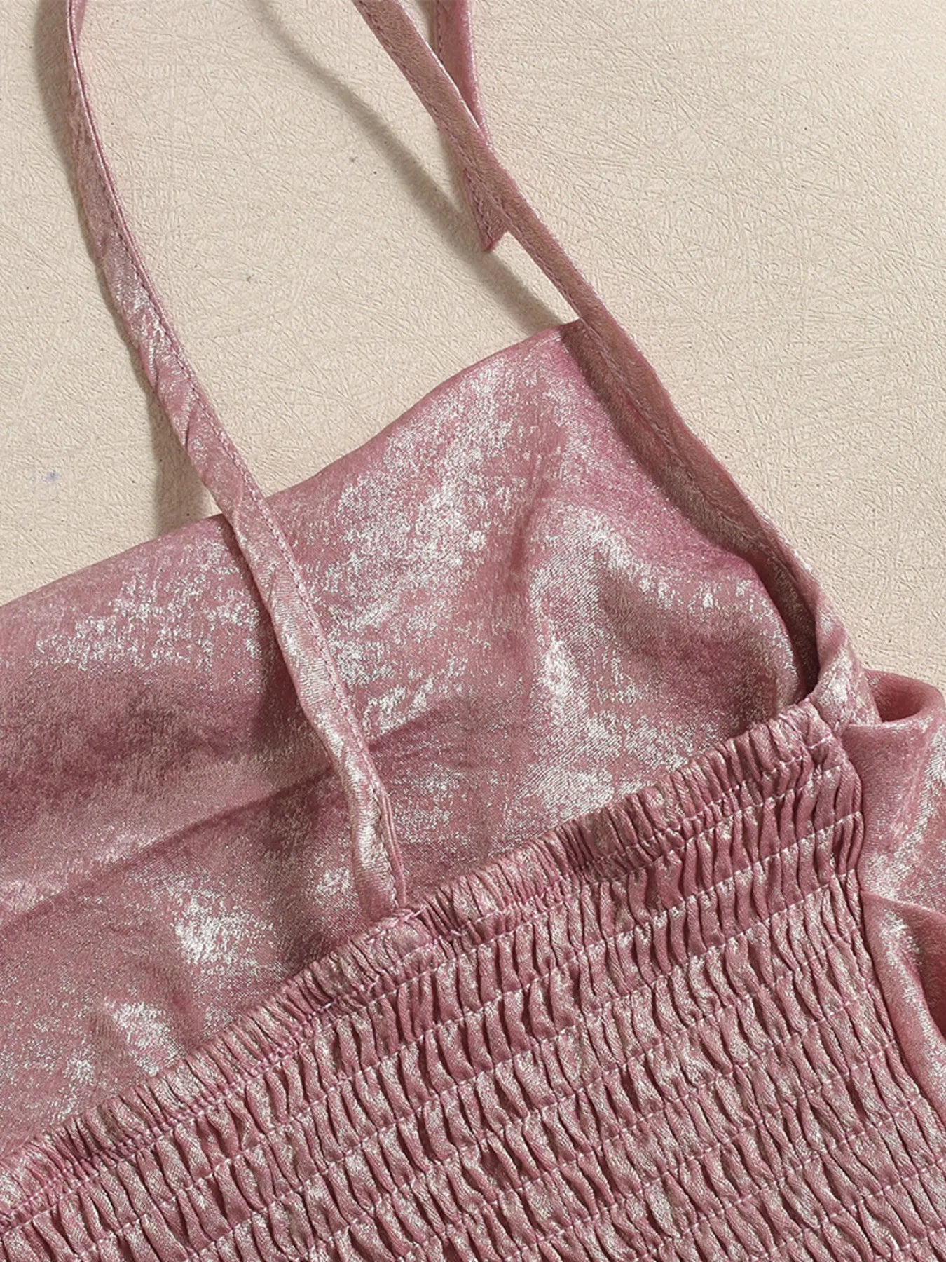 Close-up of a pink shimmery summer cami top with thin adjustable tie up straps on a beige background