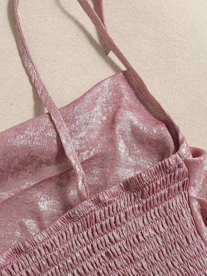 Close-up of a pink shimmery summer cami top with thin adjustable tie up straps on a beige background