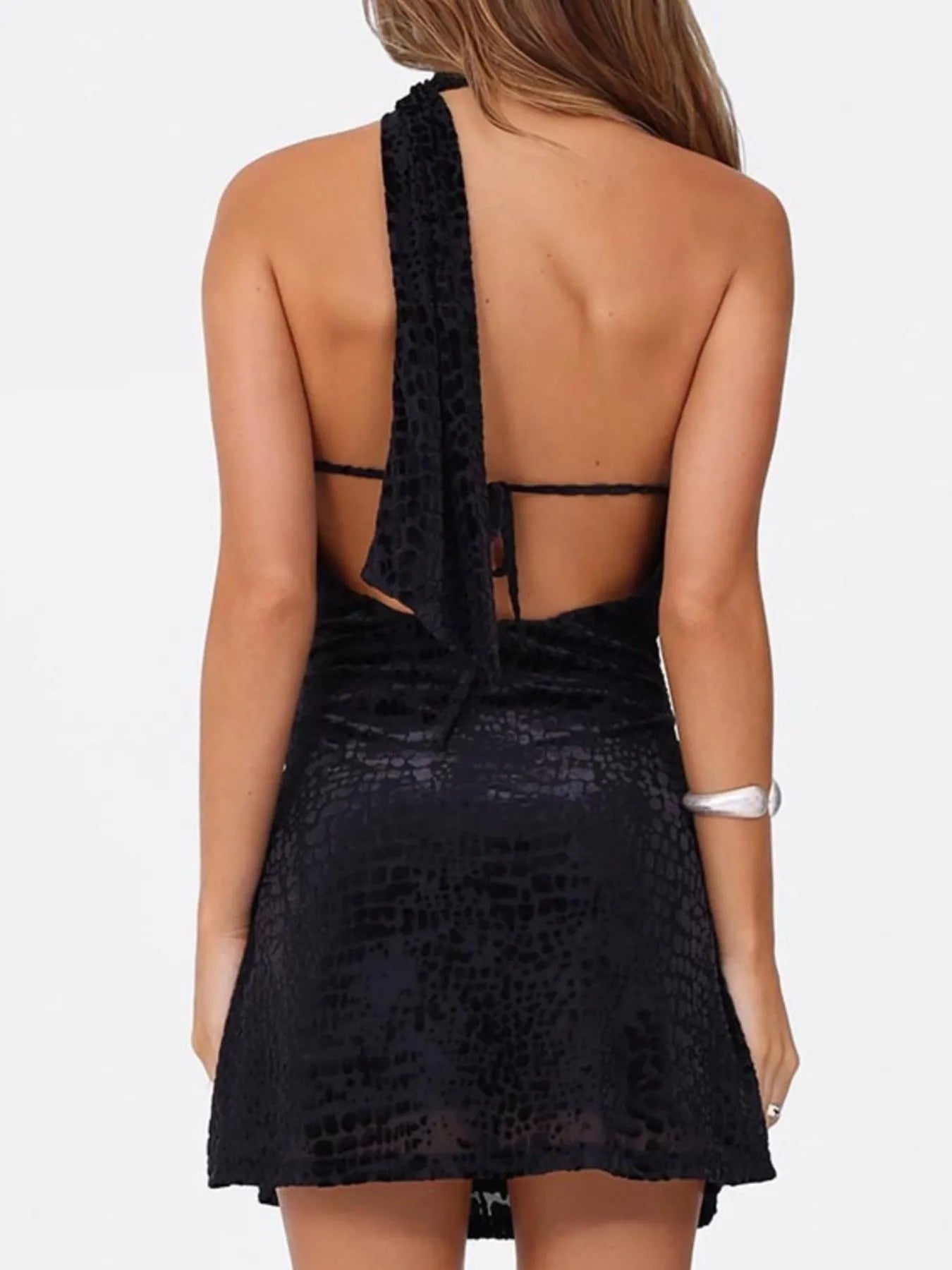 Back view of black animal patterned one shoulder halter mini dress with open back on a white background