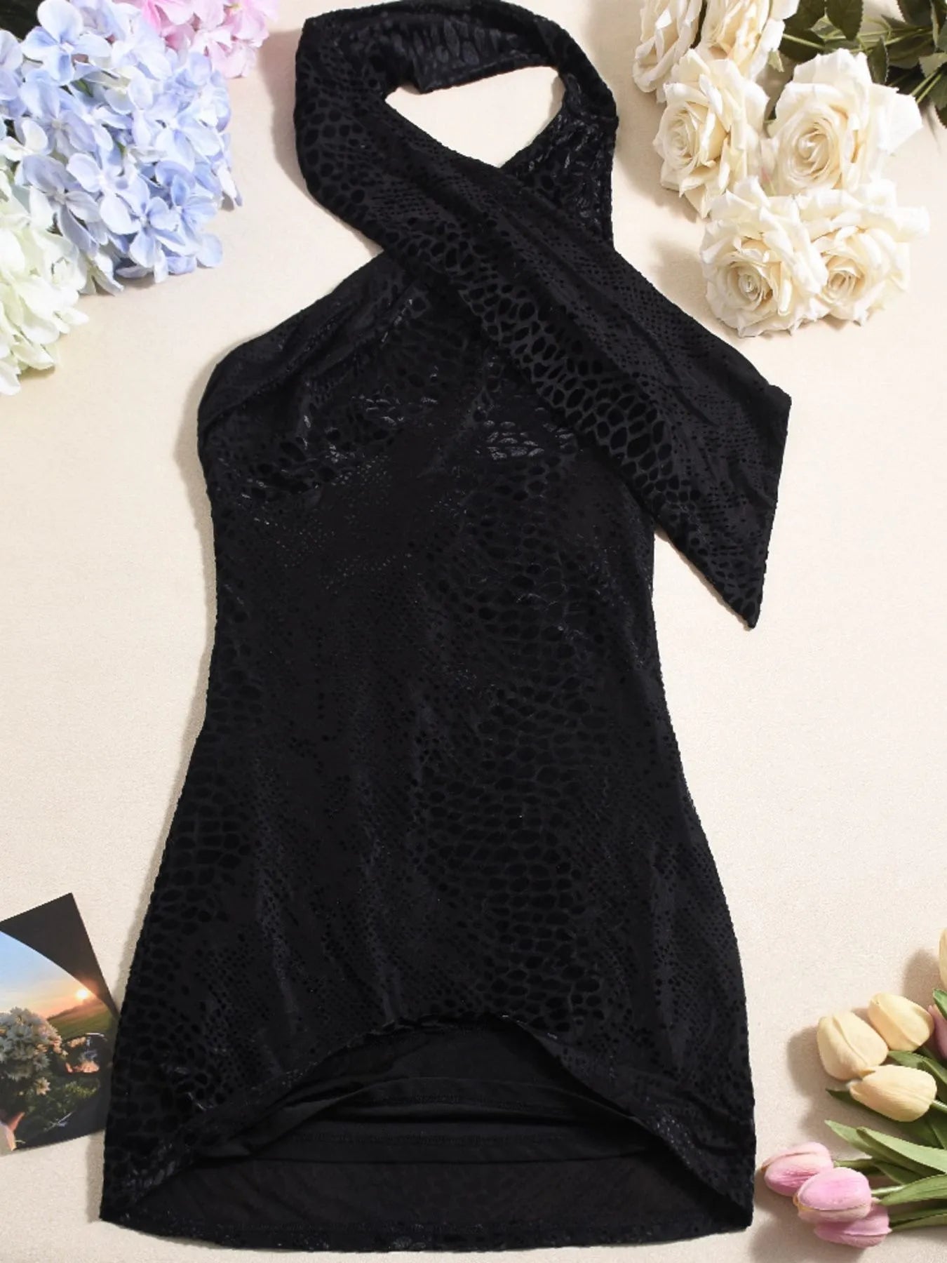 Black halter neck mini dress with lace back detailing on a light background with flowers