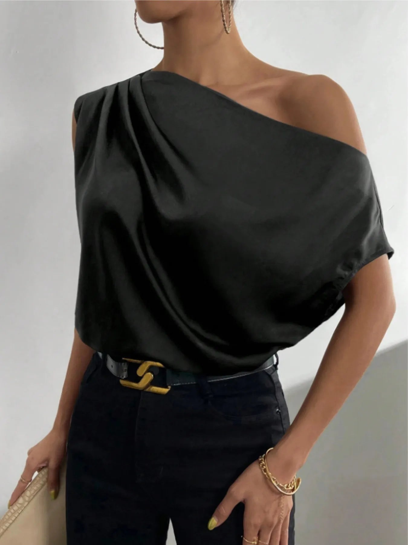 Black Asymmetrical One-Shoulder Draped Blouse worn by a woman with a belted denim pants on a plain background