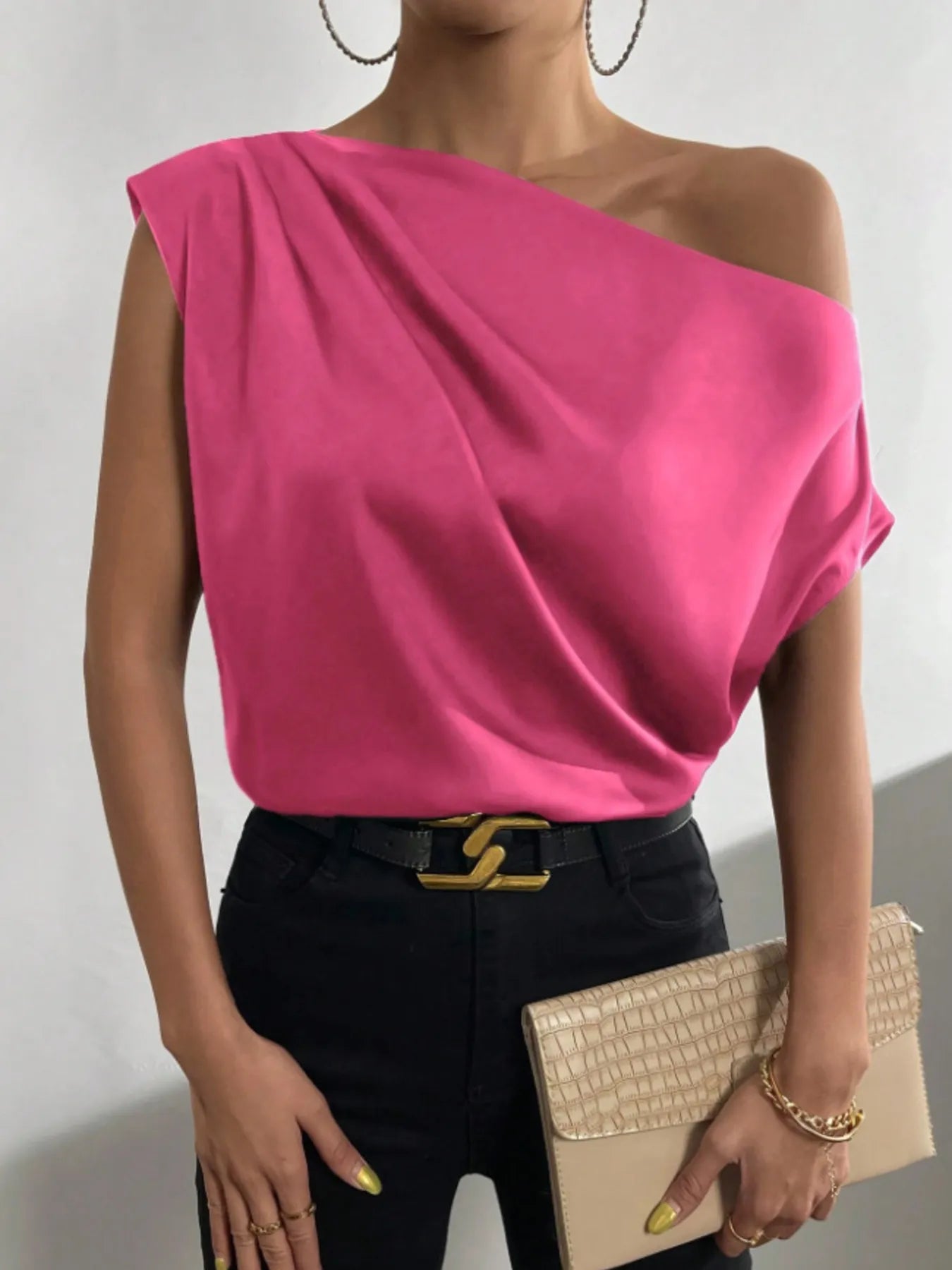 woman wearing a pink satin Asymmetrical One-Shoulder Draped Blouse with black pants and holding a beige clutch.