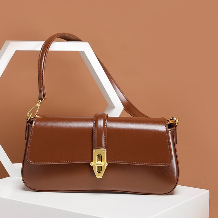 Brown genuine leather baguette handbag with gold accents on a white surface against a brown background