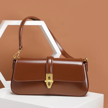 Brown genuine leather baguette handbag with gold accents on a white surface against a brown background
