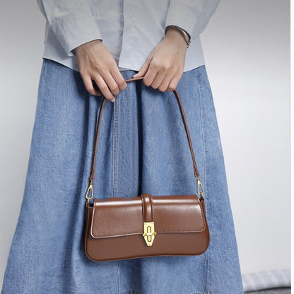 Brown genuine handbag held by a model wearing a light blue shirt and denim skirt on a plain background