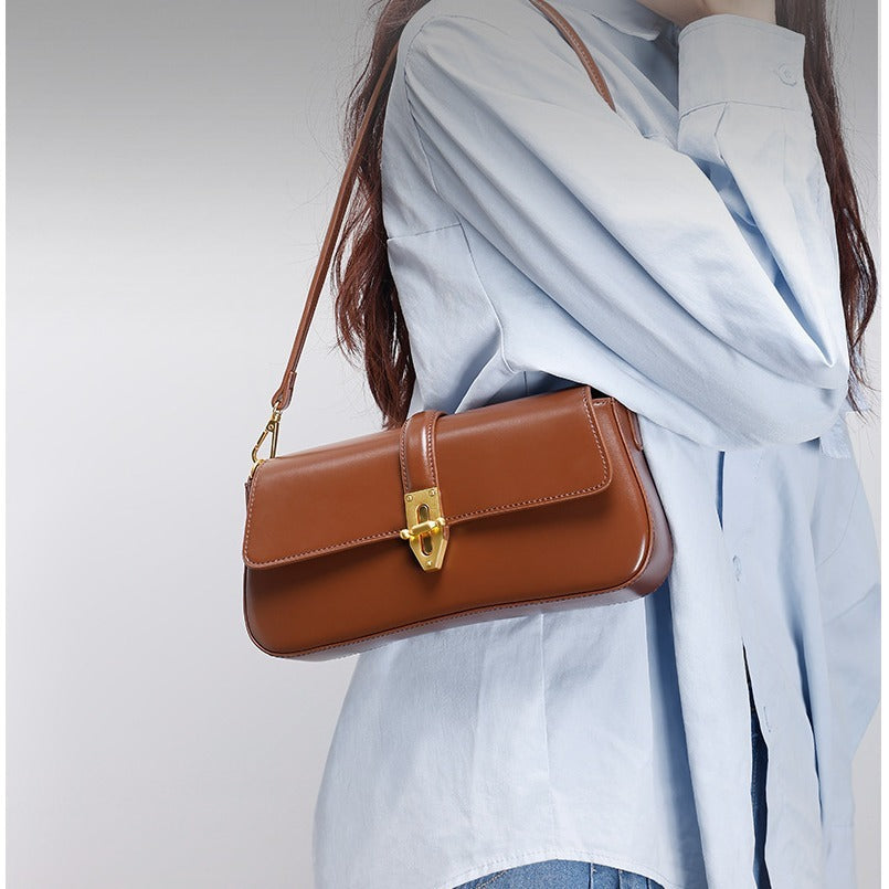 Model carrying a brown real leather shoulder handbag with gold clasp a in a light gray background