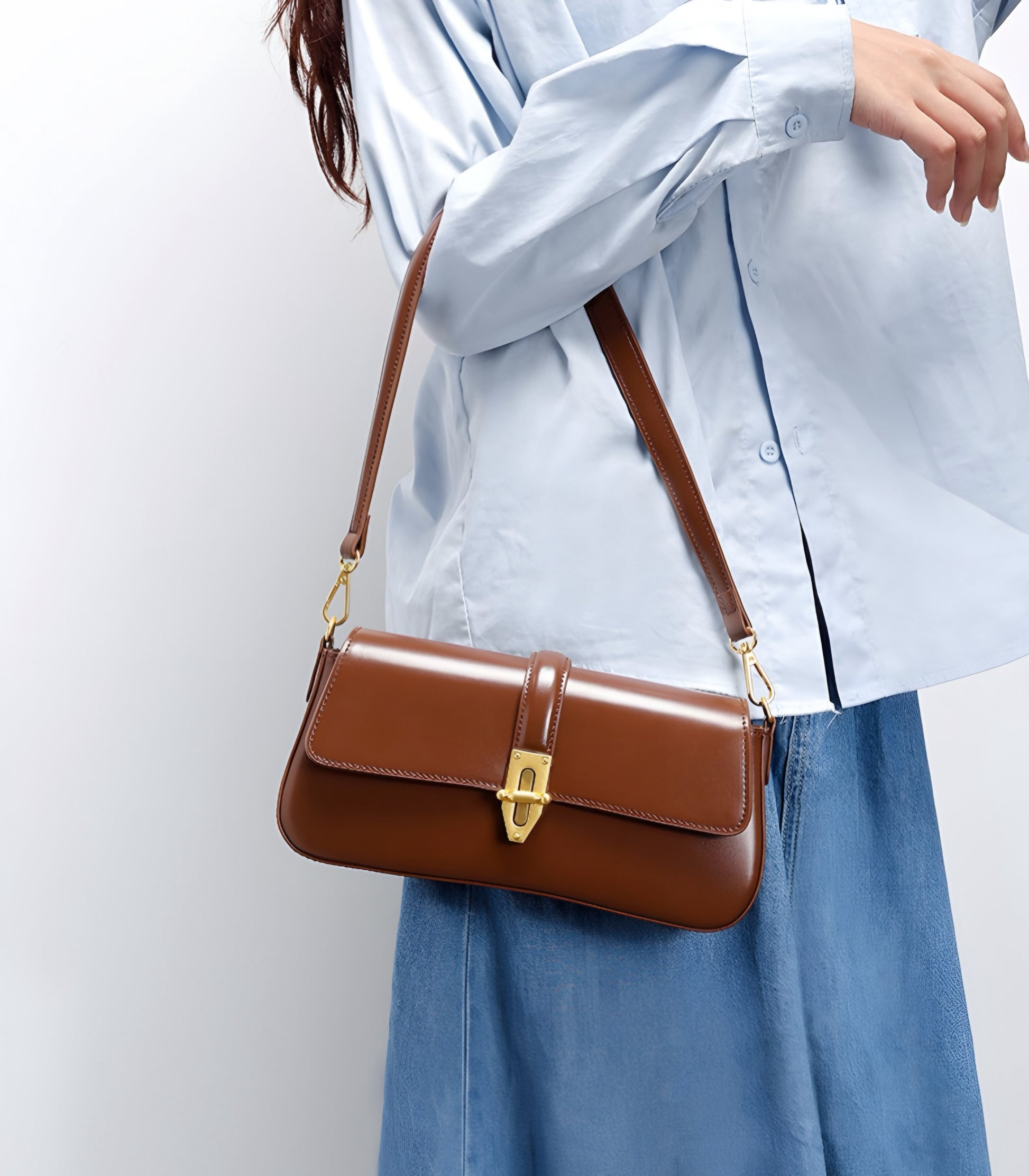 Brown genuine leather baguette handbag worn by a woman in a light blue shirt and jeans on a white background