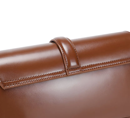 Close-up of back of a brown genuine leather baguette bag with visible stitching on a white background
