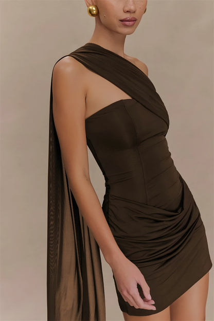 Woman wearing a brown draped one-shoulder mini dress against a beige background close up