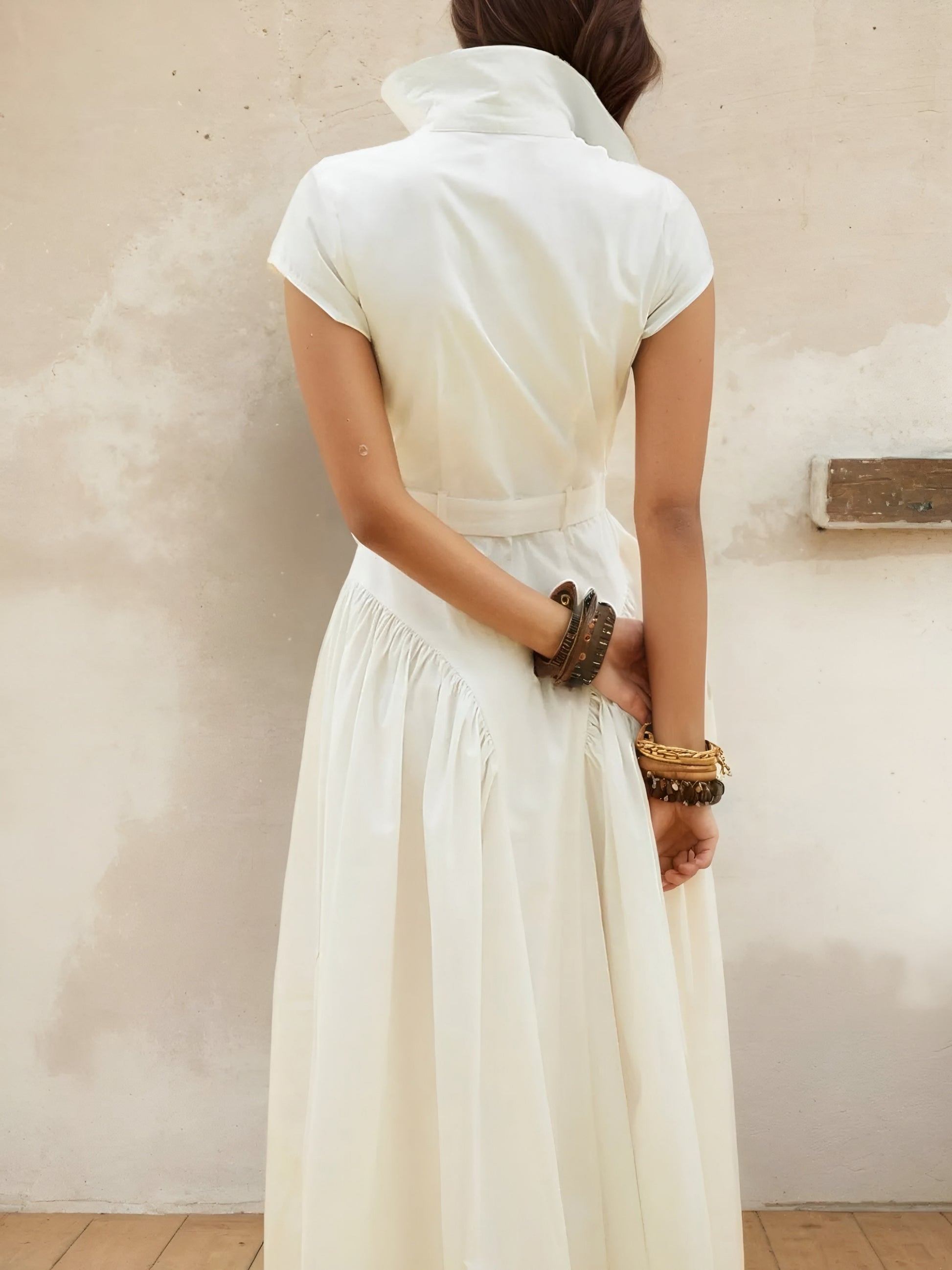 Back view of woman  wearing a white cap sleeve belted midi resort style dress with a neutral background