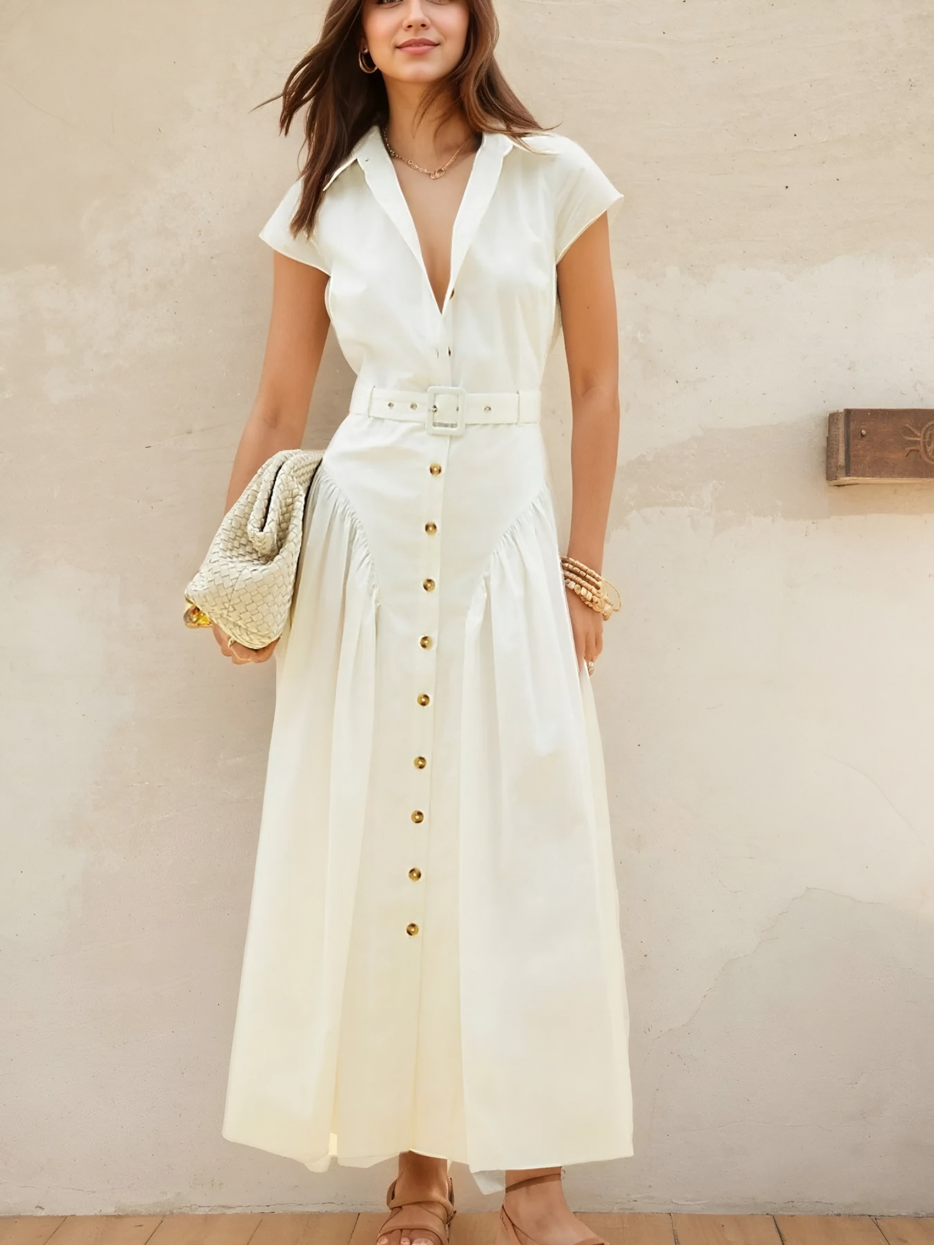 Woman wearing a white button front cap sleeve belted resort chic style casual shirt dress against a beige wall.