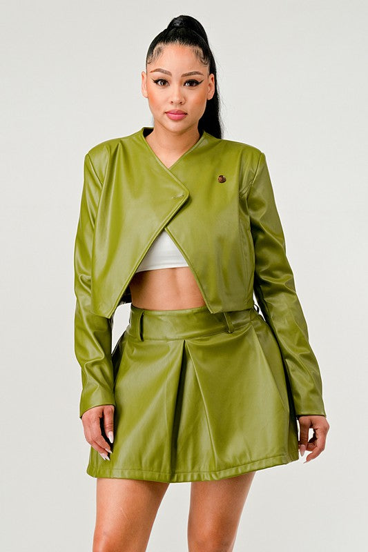 Woman wearing a chic edgy green vegan leather jacket and skirt two piece set on a plain background