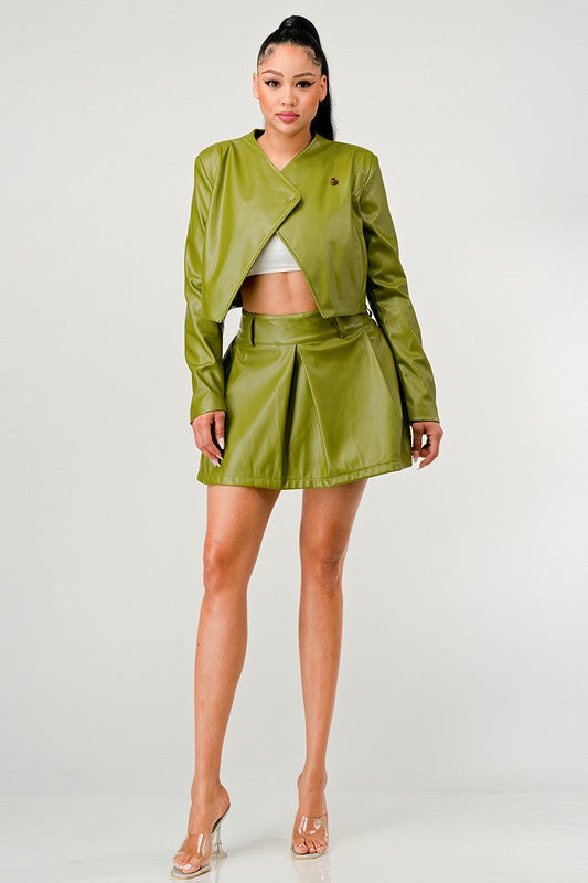 Woman wearing a green leather asymmetrical jacket and pleated skirt outfit set on a white background