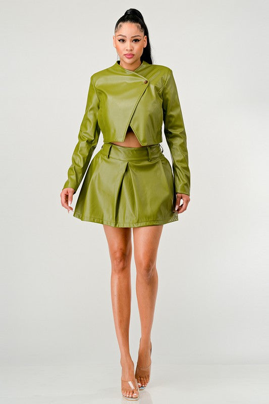 Woman wearing a green leather button-up PU leather cropped jacket with pleated skirt on a white background