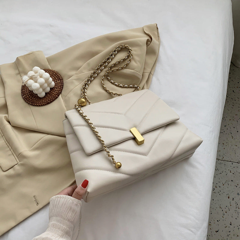 Beige quilted chain chevron shoulder bag with gold clasp with coat background
