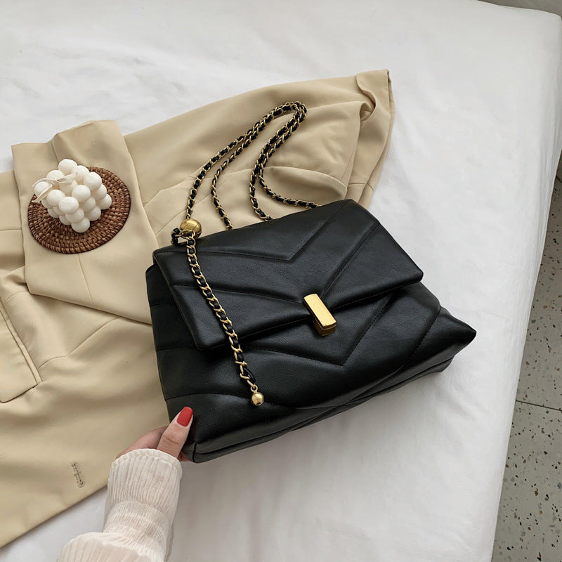 Black quilted chain chevron shoulder bag with gold clasp with coat background