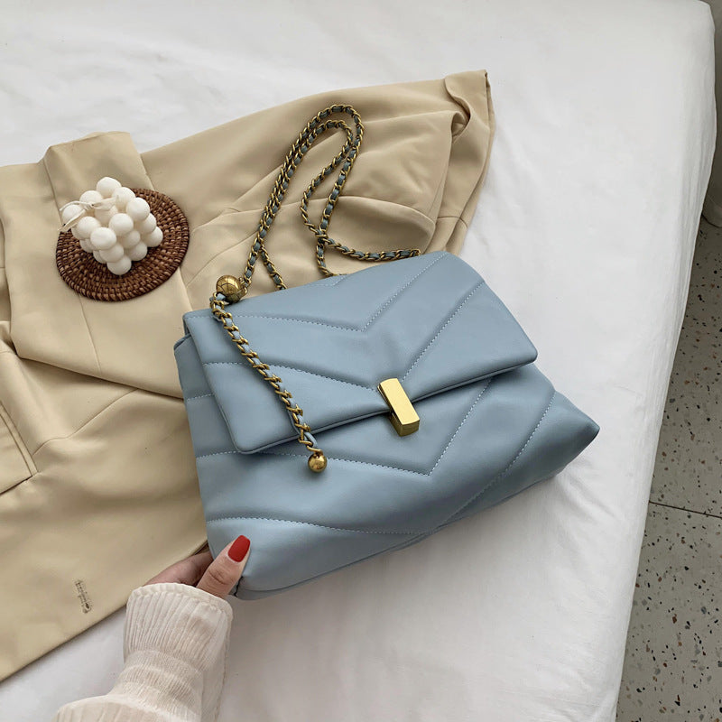 Blue quilted chain chevron shoulder bag with gold clasp with coat background